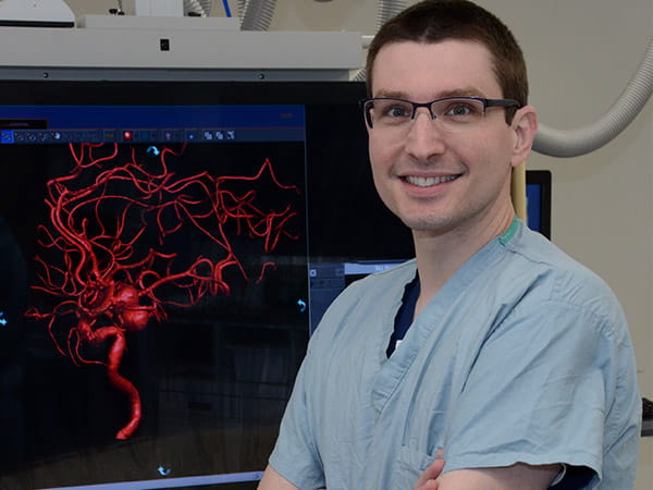 Dr. Kimon Bekelis is smiling next to a digital image in a medical room.